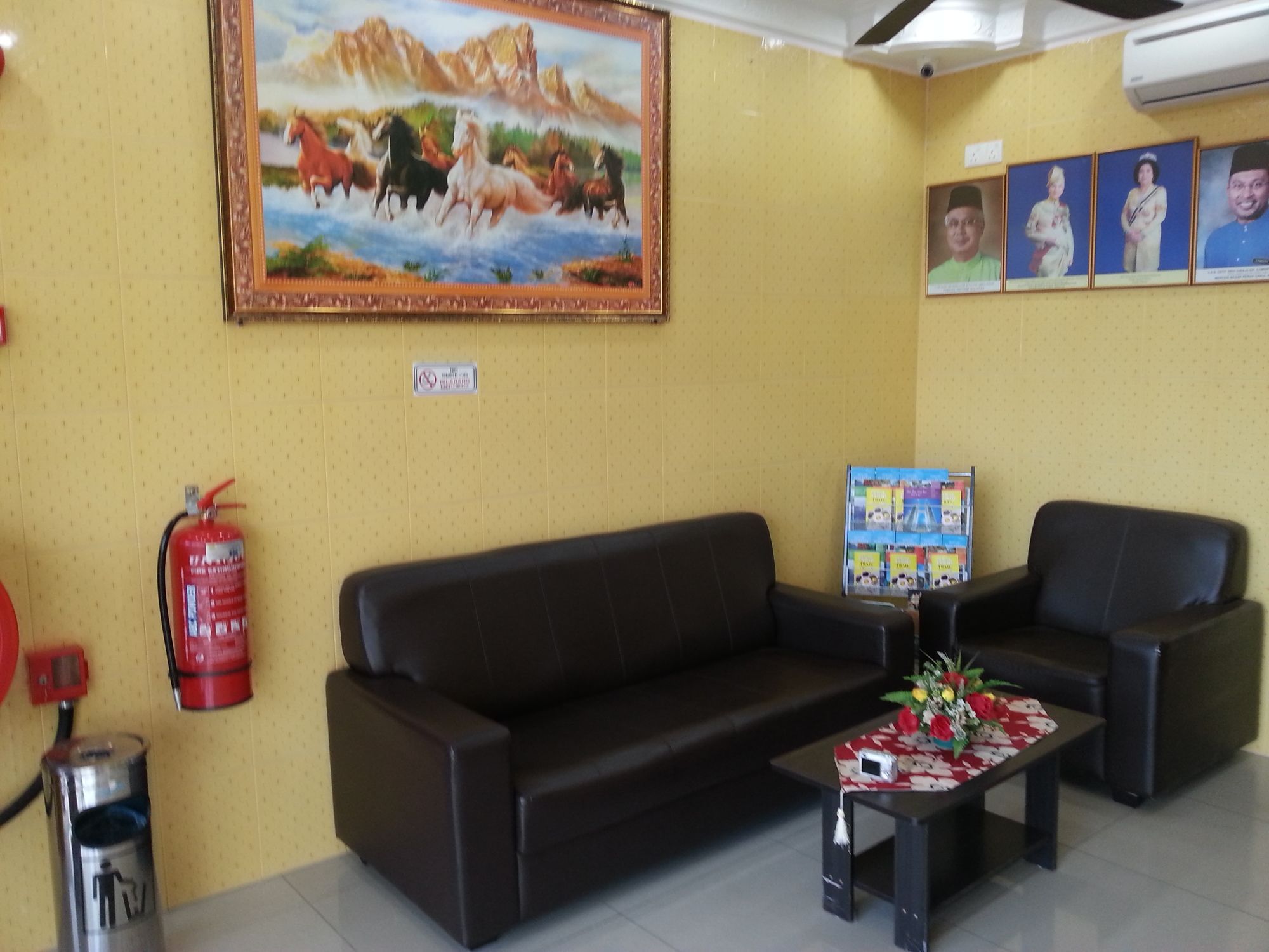 A lobby with a sofa, chairs, a fire extinguisher, a fire alarm, a painting, and a wall-mounted display.