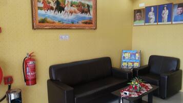 A lobby with a sofa, chairs, a fire extinguisher, a fire alarm, a painting, and a wall-mounted display.