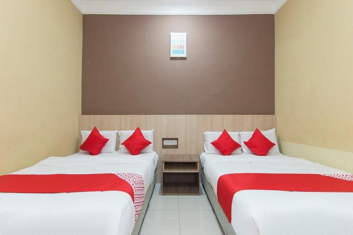 Ein Hotelzimmer mit zwei Betten, jeweils mit weißer Bettwäsche und roten Kissen, einem kleinen Nachttisch und einer wandmontierten Leuchte.