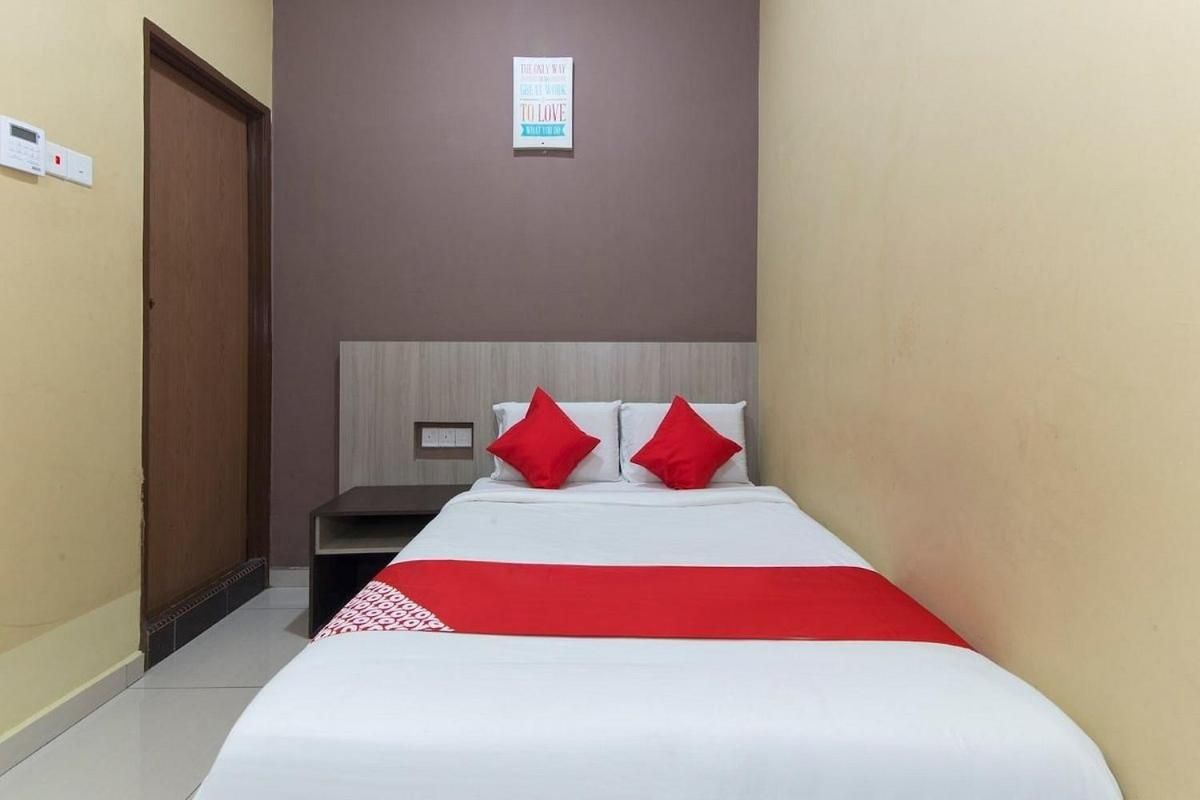 Una habitación de hotel con una cama, una mesita de noche, una manta roja y un letrero en la pared.