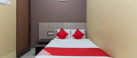 Una habitación de hotel con una cama, una mesita de noche, una manta roja y un letrero en la pared.