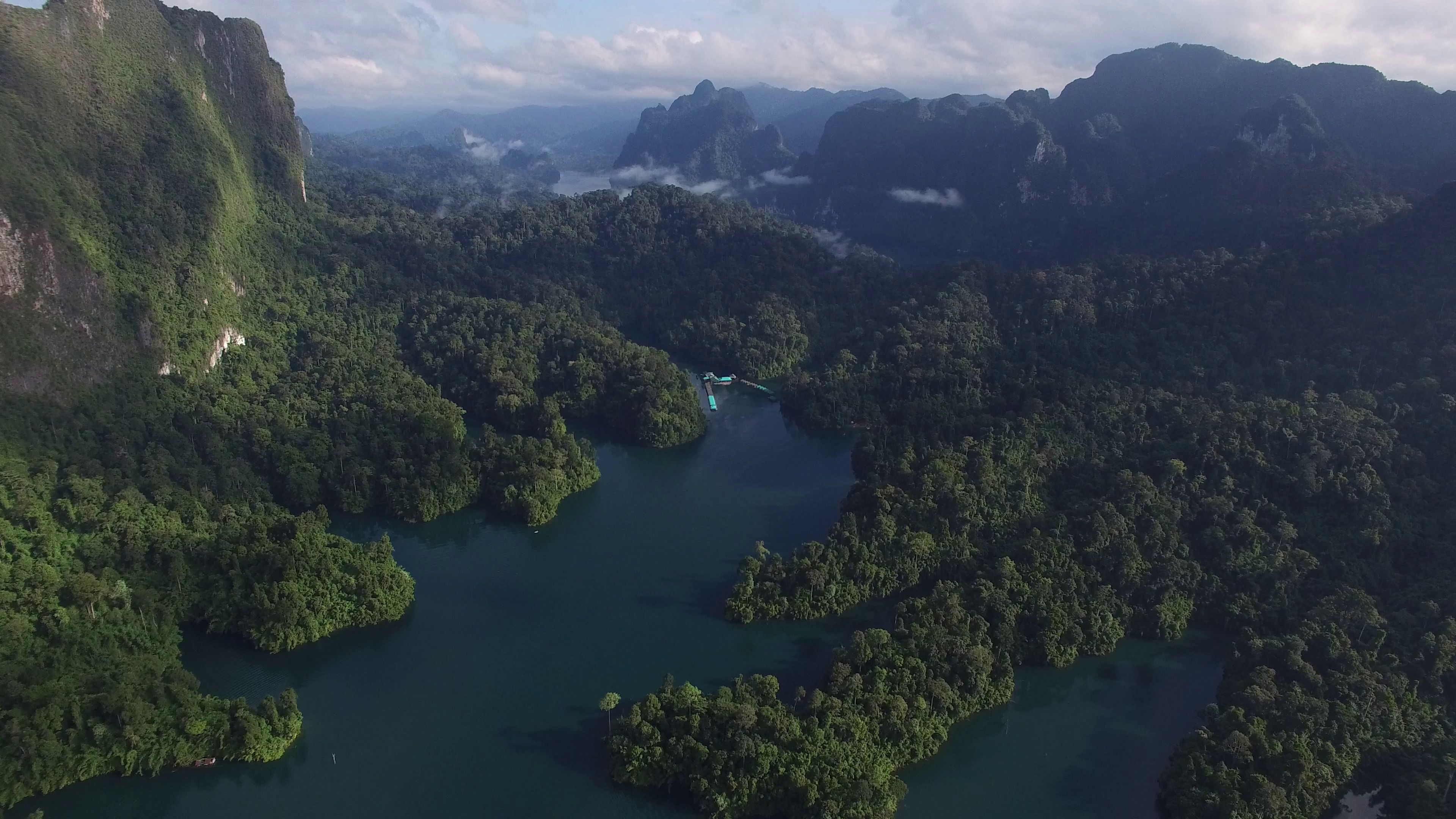 Vista aérea de un valle exuberante y verde, con un río serpenteando a través de él, rodeado de un bosque denso y montañas al fondo.