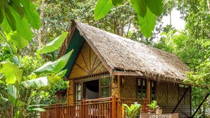 Une petite cabane à toit de chaume, portant l’inscription « Hibiscus 2 », est entourée d’une végétation luxuriante.