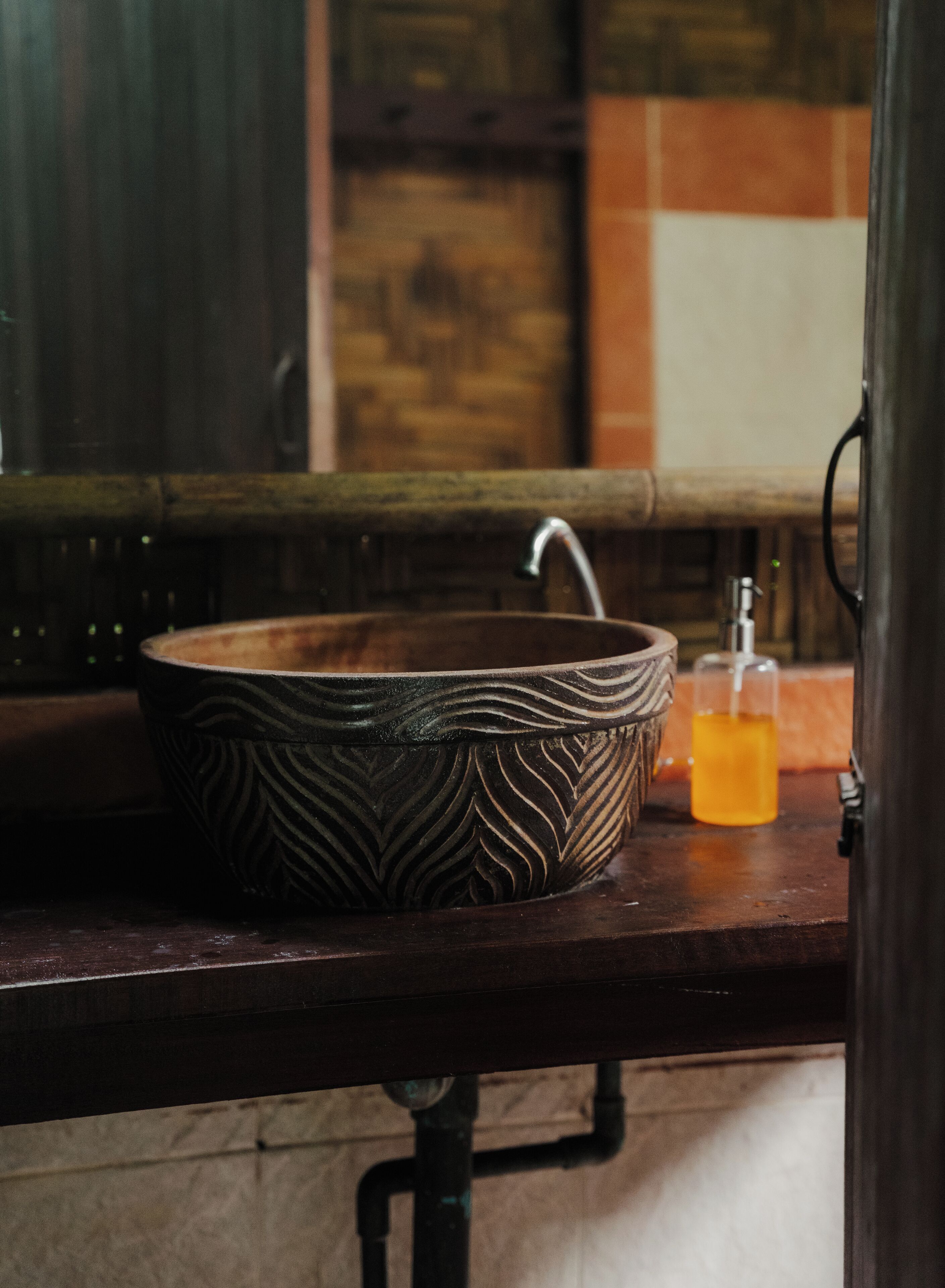 A wooden bowl sink with a faucet, a glass bottle with a yellow liquid, and a wooden countertop.