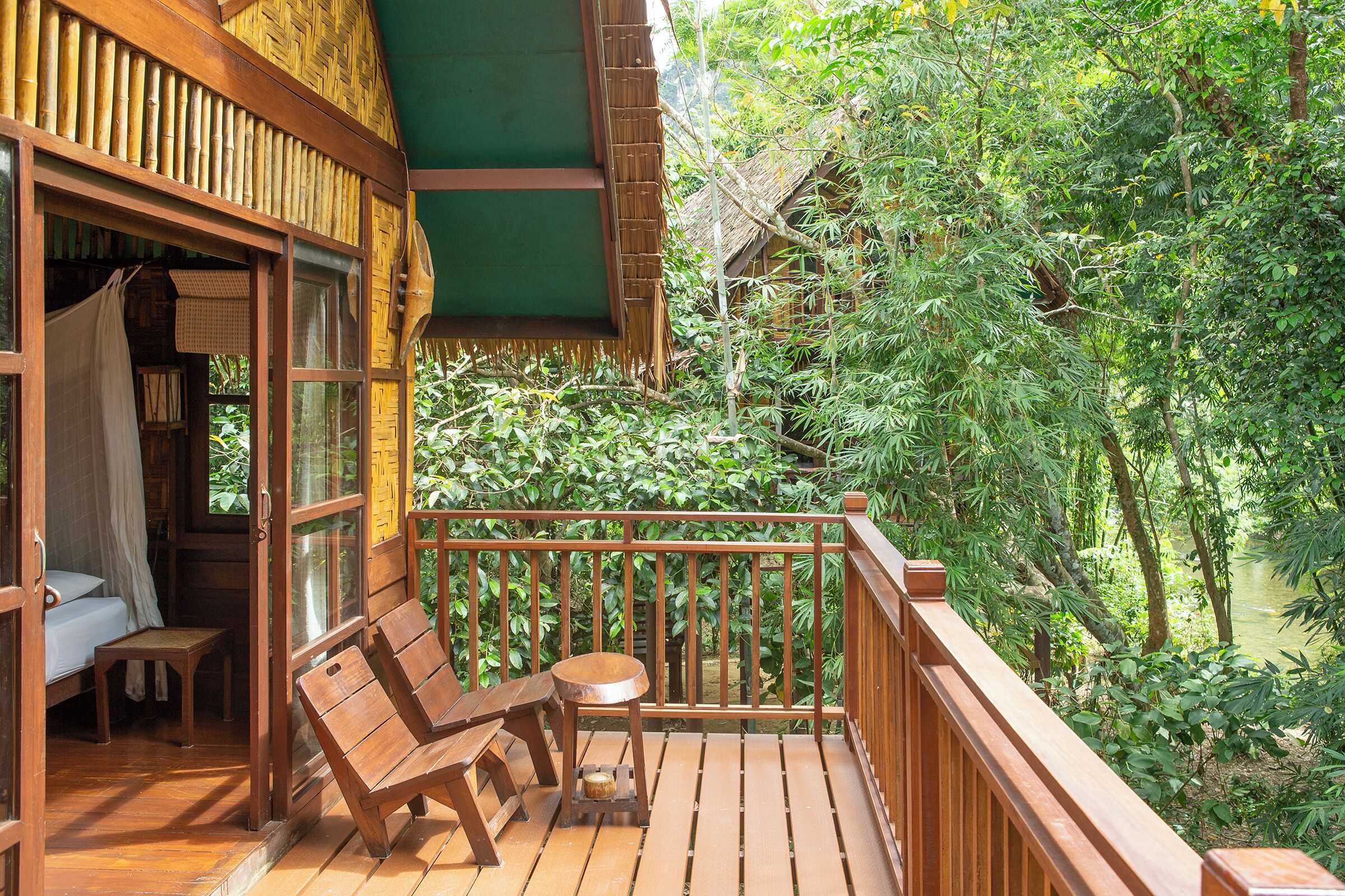 Une terrasse en bois avec un banc et une table en bois, entourée d’une végétation luxuriante et d’une structure en bambou.