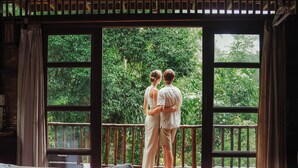 A couple standing on a balcony with a bed and towels in the foreground.