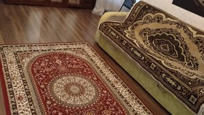 A living room with a wooden cabinet, a patterned sofa, and a red and beige rug. - Apartments Galactika (Uralsk)