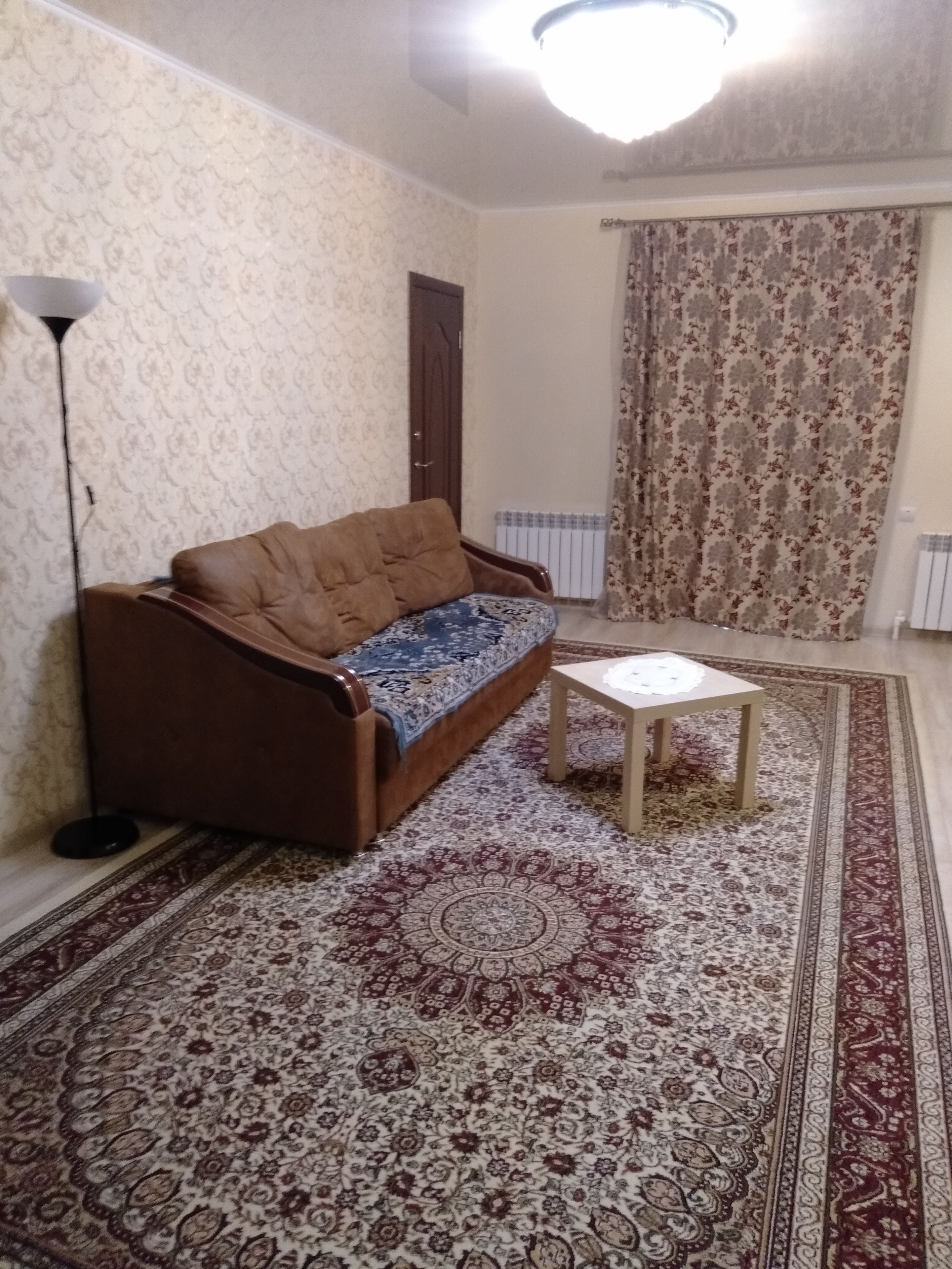 A living room with a brown sofa, a small table, and a patterned rug.