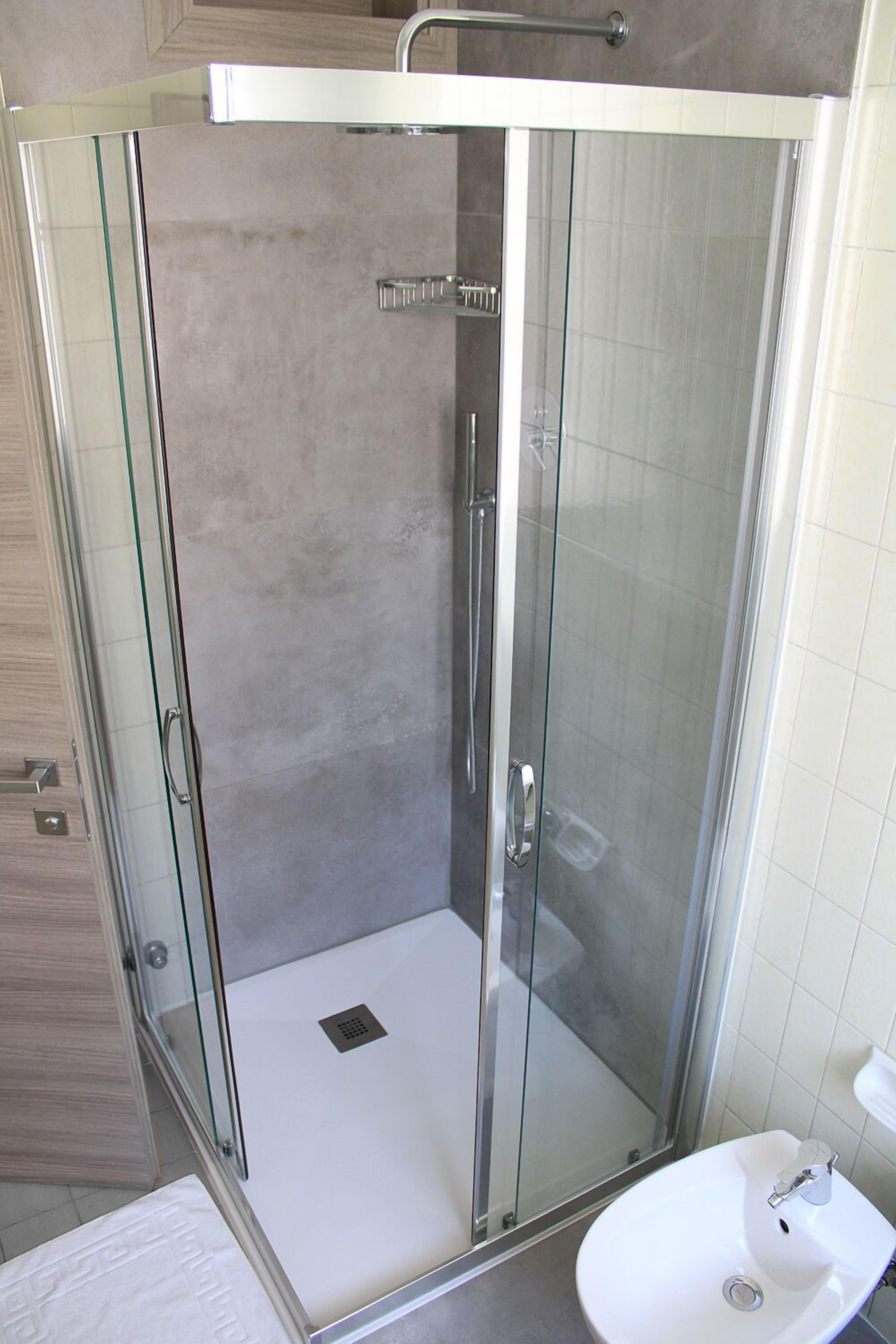 A glass-enclosed shower with a white sink and a towel rack.