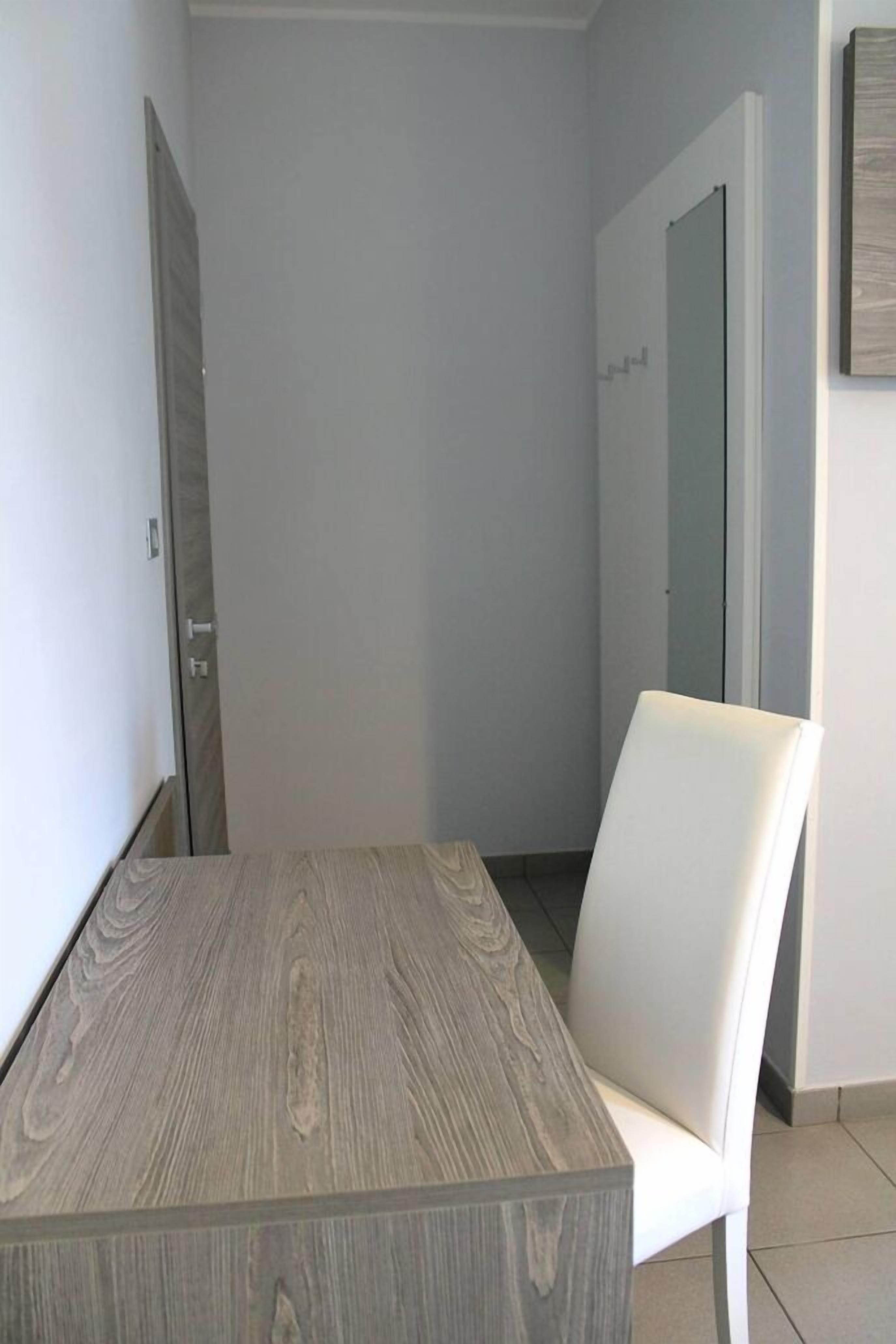 A modern room with a wooden table and a white chair, a door, and a mirror on the wall.