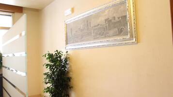 A hallway with a framed picture on the wall, a staircase, and a potted plant.