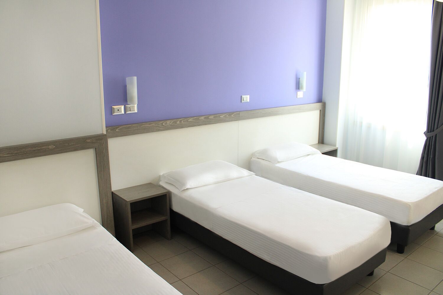 Habitación de hotel con dos camas individuales, una mesita de noche, un cabecero de madera y una pared de acento morada.