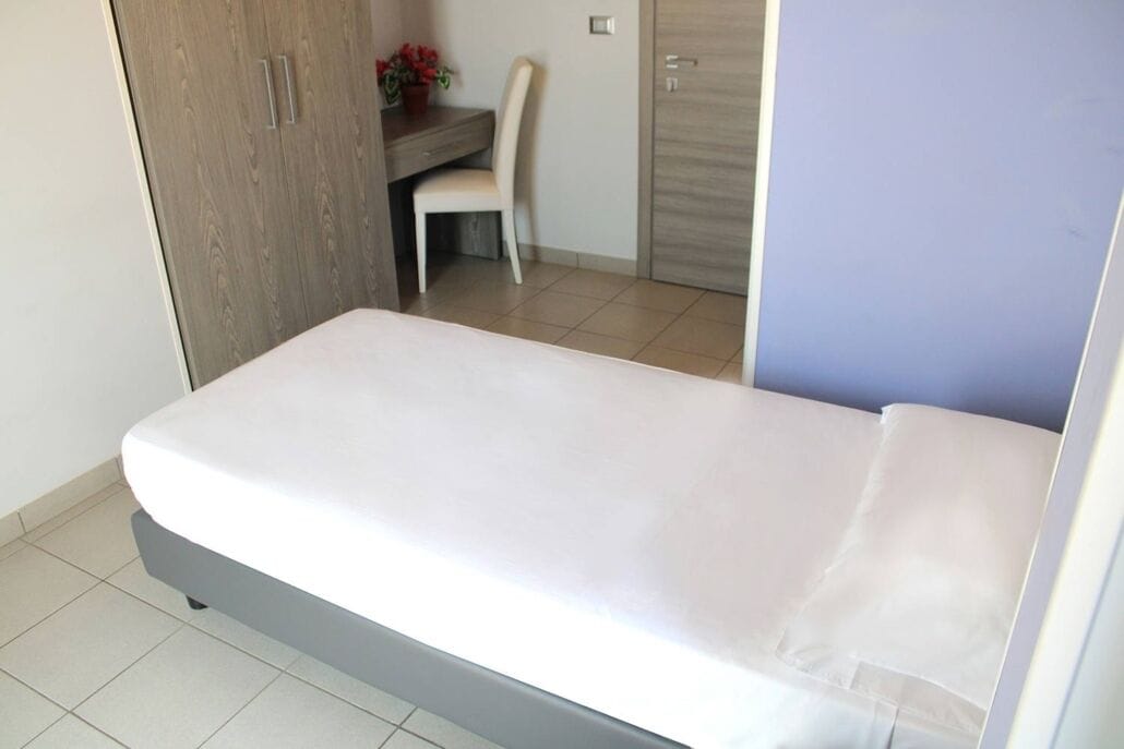 A small, neatly arranged bedroom with a single bed, a desk, and a chair.