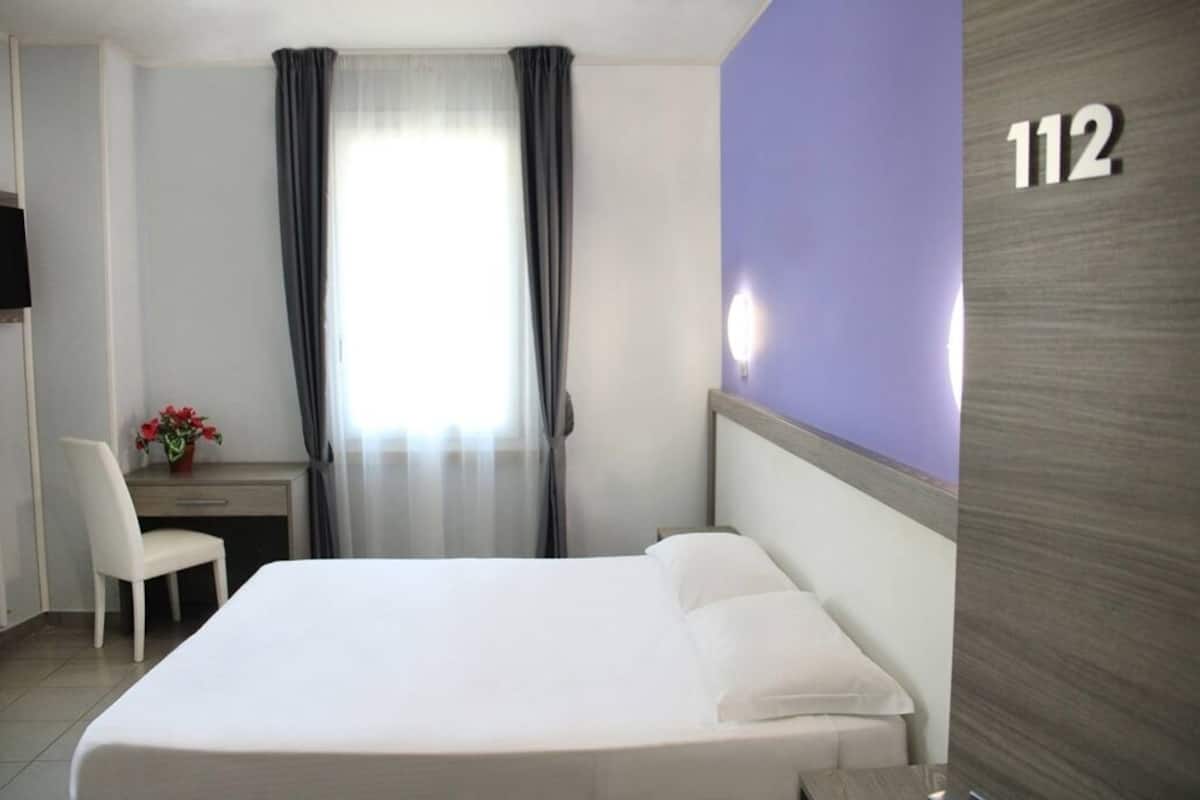 A hotel room with a bed, a desk, a chair, and a window with curtains.