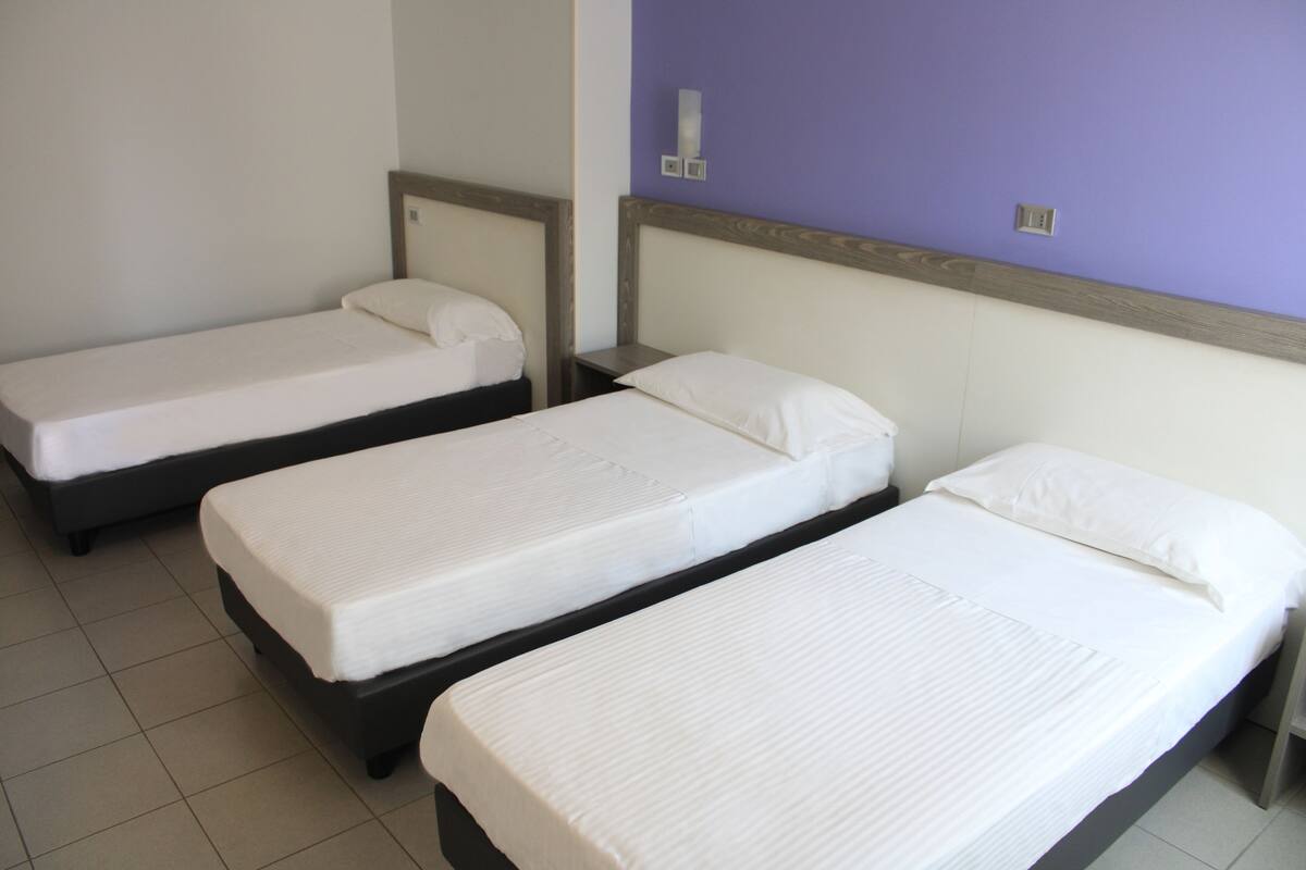 A hotel room with three single beds, each with a wooden headboard and white bedding.