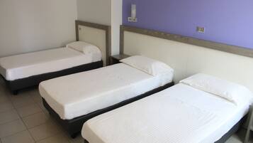 A hotel room with three single beds, each with a wooden headboard and white bedding.