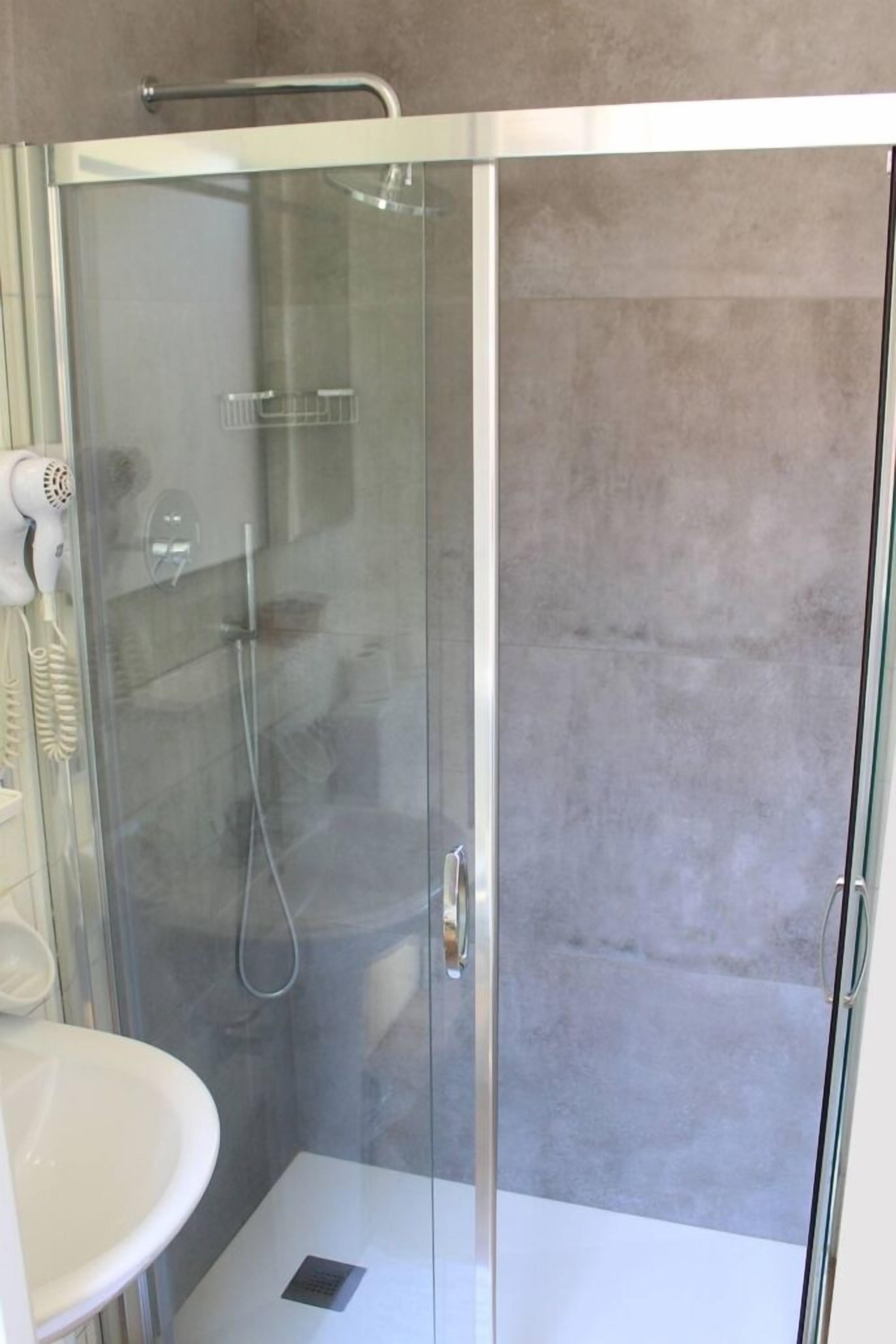 A glass-enclosed shower with a handheld dryer, a white sink, and a shower control panel.
