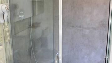 A glass-enclosed shower with a handheld dryer, a white sink, and a shower control panel.
