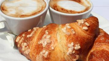Deux tasses de café décorées avec des motifs en latte art et un croissant aux noix, le tout présenté sur une assiette blanche.