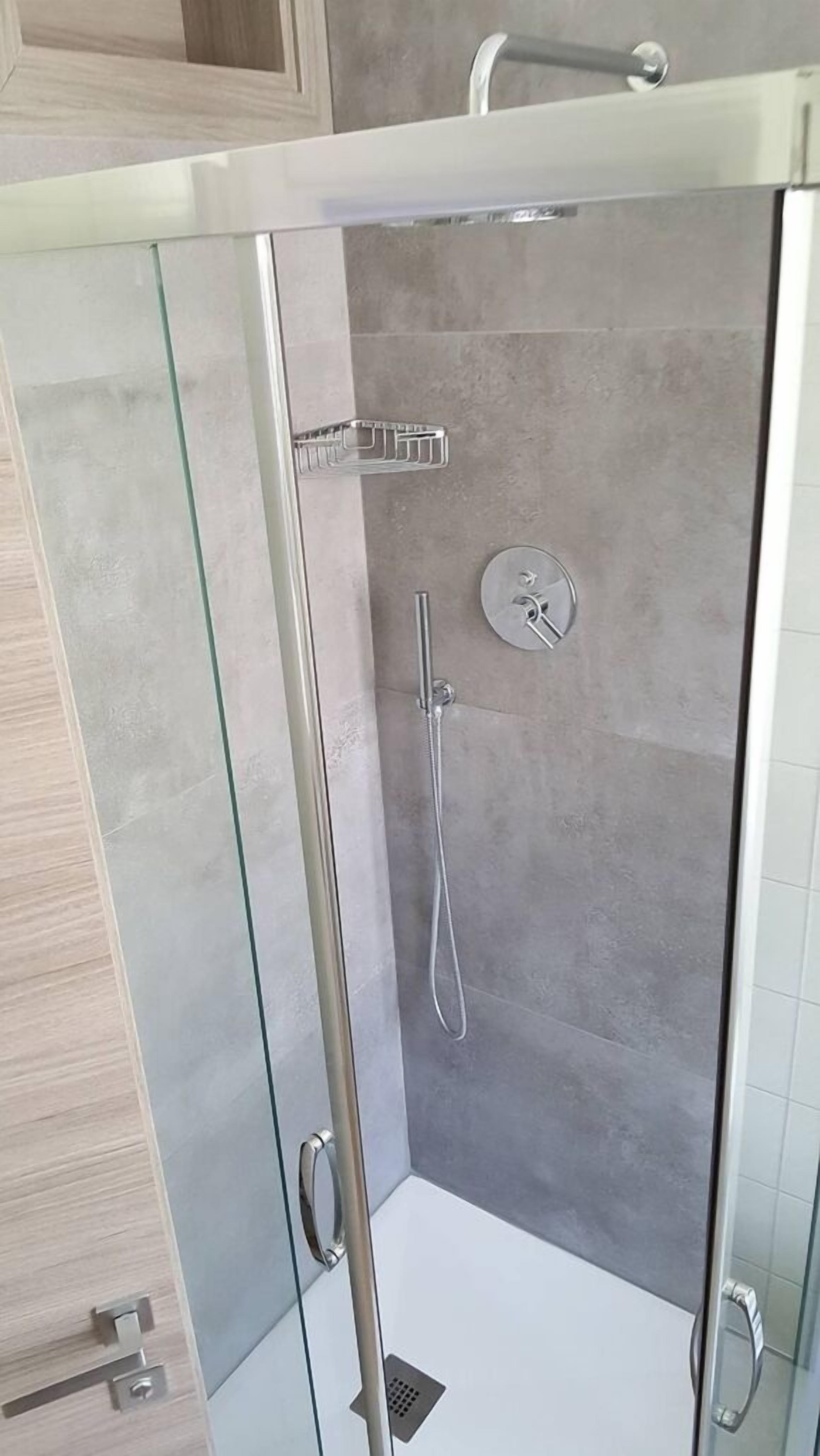 A glass-enclosed shower stall with a handheld showerhead and a wall-mounted control panel.