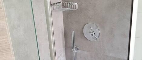 A glass-enclosed shower stall with a handheld showerhead and a wall-mounted control panel.
