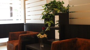 A seating area with two cushioned chairs and a small table, a vase with flowers, and a potted plant on a shelf. - Hotel Savoia (Poggio Rusco)