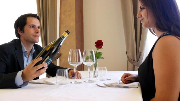 A dining table set with wine glasses and a bottle of wine, a rose in a vase, and a man holding a wine bottle. - Hotel Savoia (Poggio Rusco)