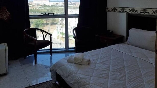 A hotel room with a large window, a bed, a chair, and a small table. - Hotel Ikram (Algiers)