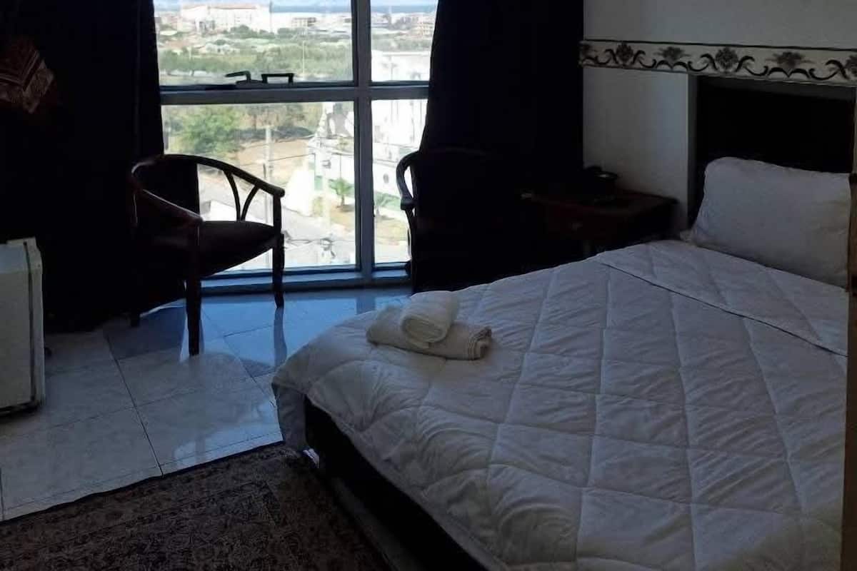 A hotel room with a large window, a bed, a chair, and a small table.