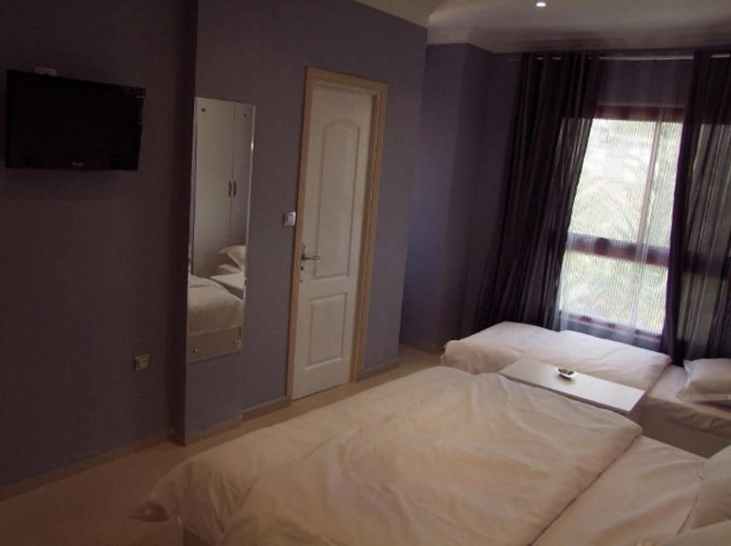 A bedroom with two beds, a wardrobe, a television, and a window with curtains.