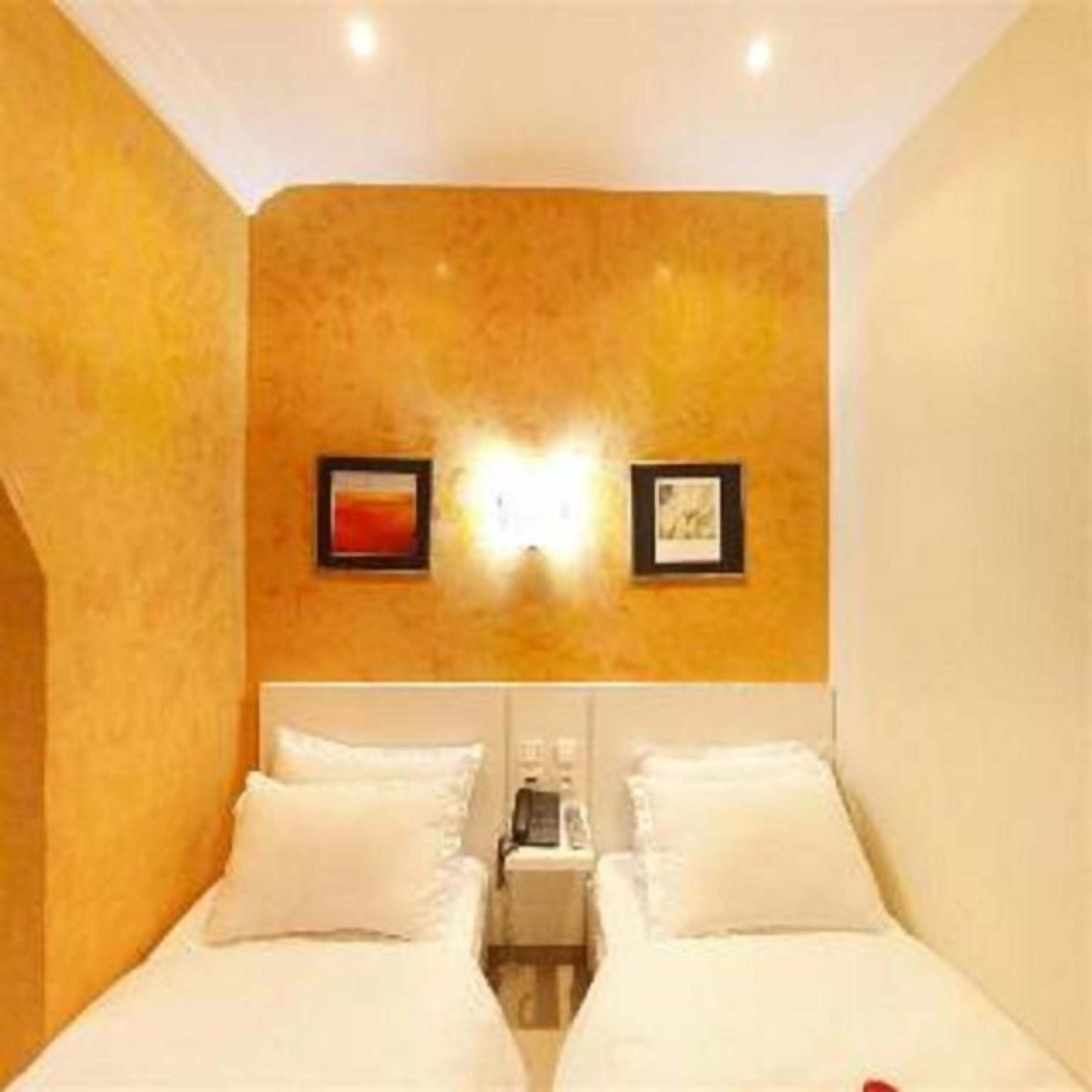 A hotel room with two beds, a nightstand, and wall-mounted lighting.