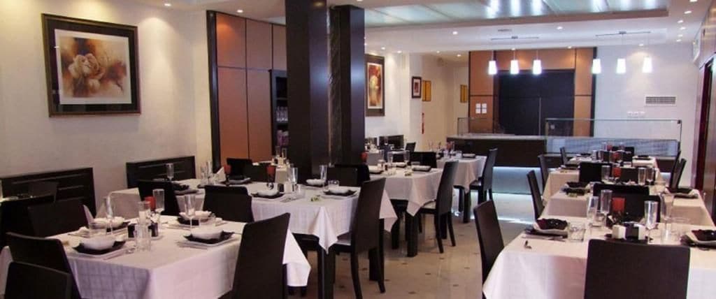 Un restaurante con varias mesas y sillas, una cocina al fondo y cuadros en las paredes.