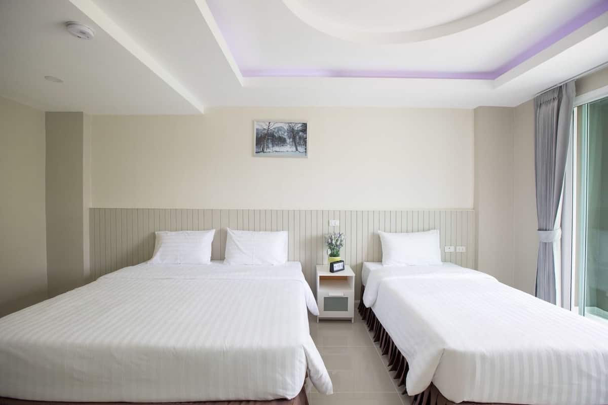 A hotel room with two beds, a nightstand with a clock, a small table with a vase, and a painting on the wall.