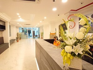A hotel reception area with a marble floor, a reception desk, and a large floral arrangement.