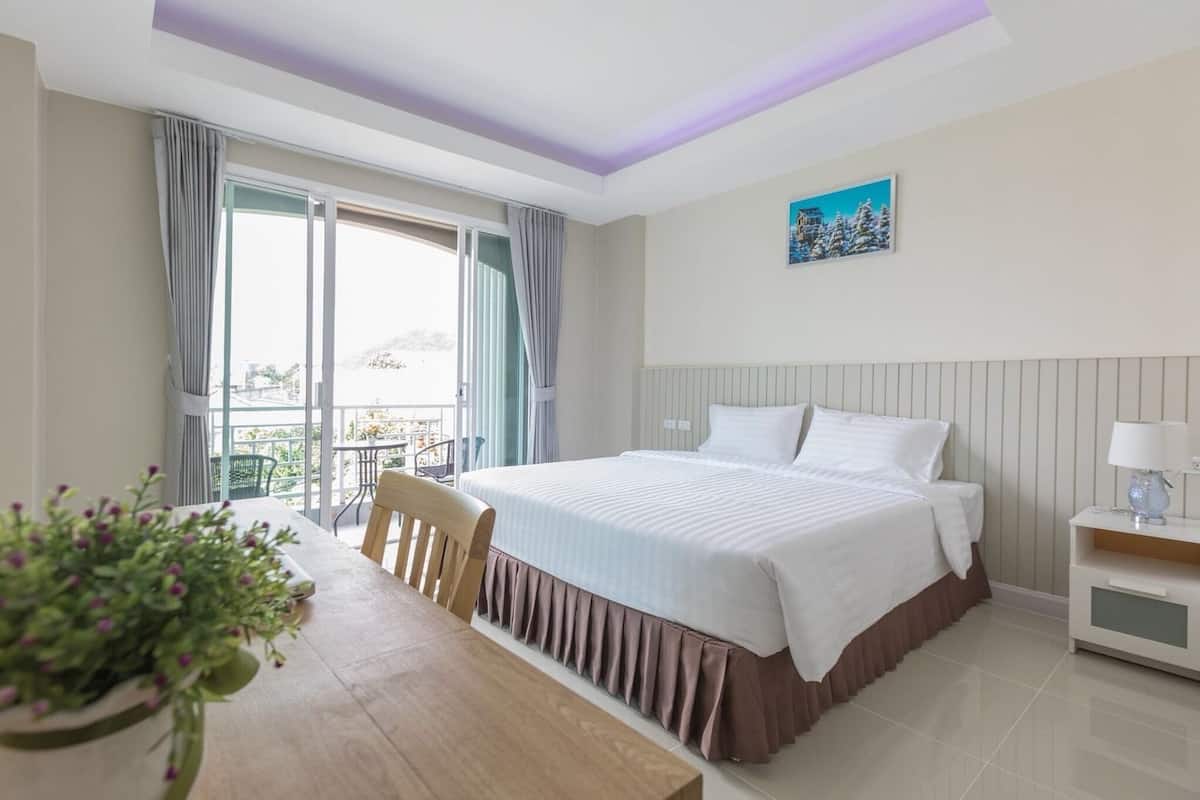 A hotel room with a bed, a table with chairs, a potted plant, a nightstand, and a view of the outdoors.