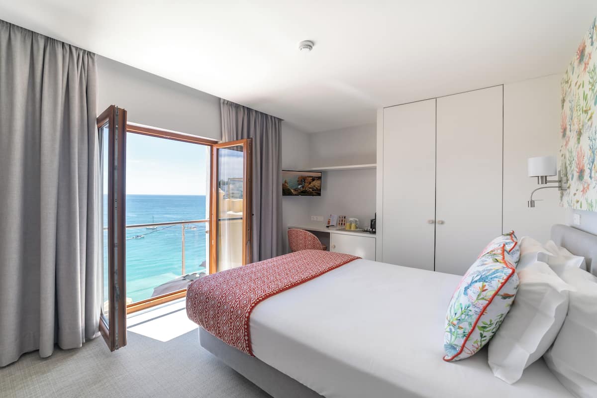 A hotel room with a bed, a desk, and a view of the sea.