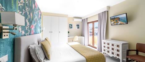 A hotel room with a bed, a desk, a chair, a dresser, and a large window with curtains.