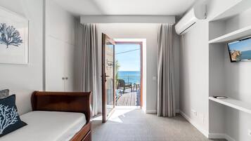 Un dormitorio con una cama, un televisor en una repisa y vista al mar a través de una puerta abierta.