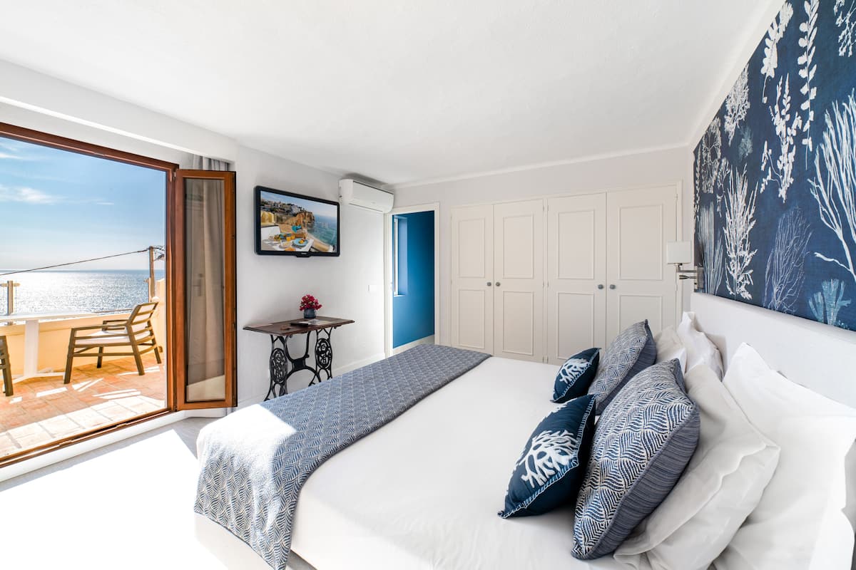A bedroom with a large bed, a view of the sea, a balcony, and a dining area.