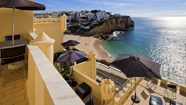Un balcon avec coin salon extérieur, offrant une vue sur une plage et une ville perchée sur une falaise.
