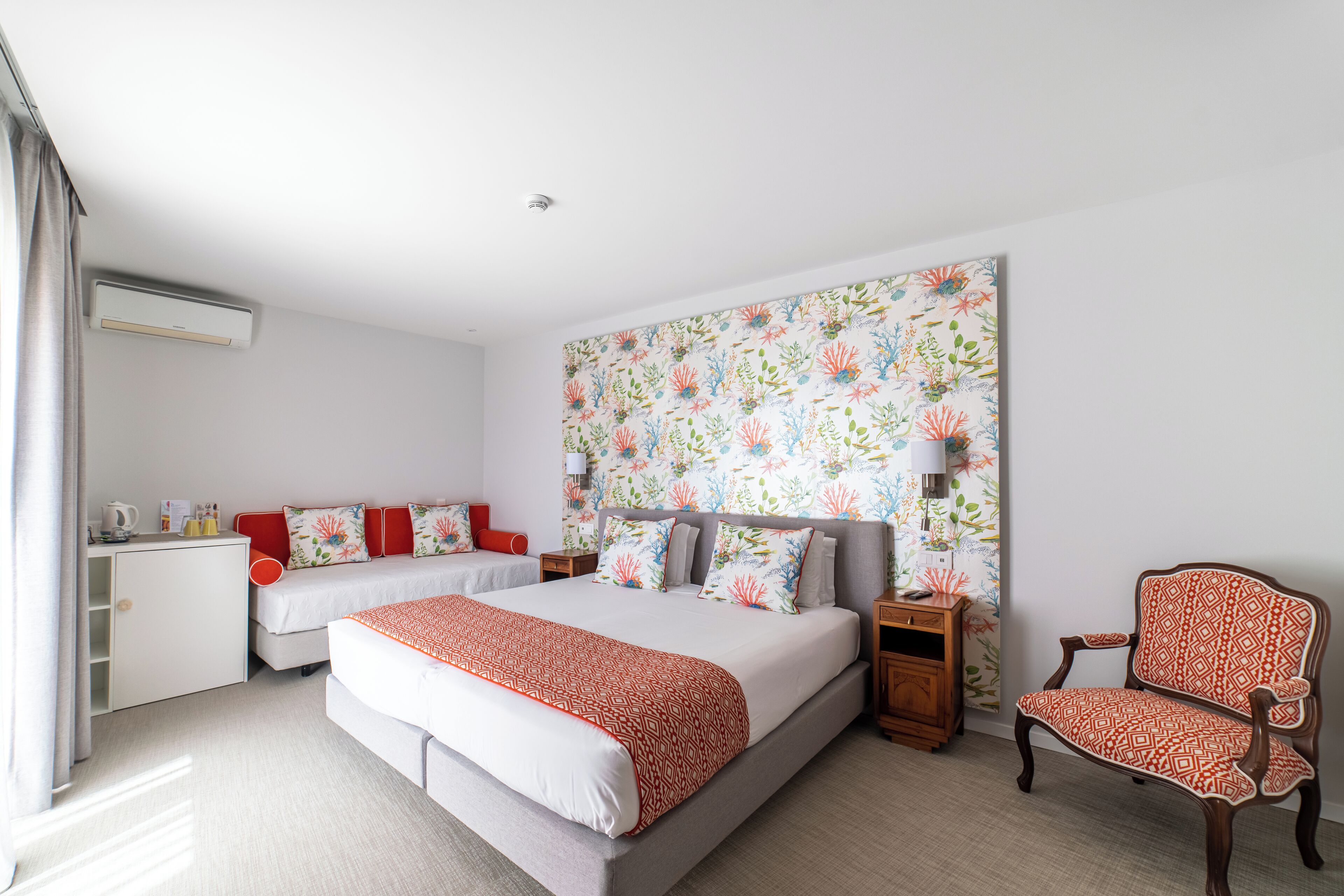 A hotel room with two beds, a desk, a chair, and a large floral-patterned headboard.
