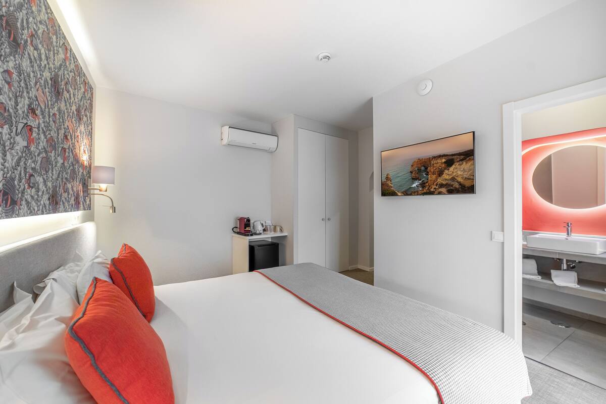 A modern hotel room with a neatly made bed, a bathroom with a vanity and sink, and a painting on the wall.