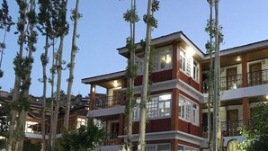 Un hotel de varios pisos con balcones, una pared blanca al frente y árboles.