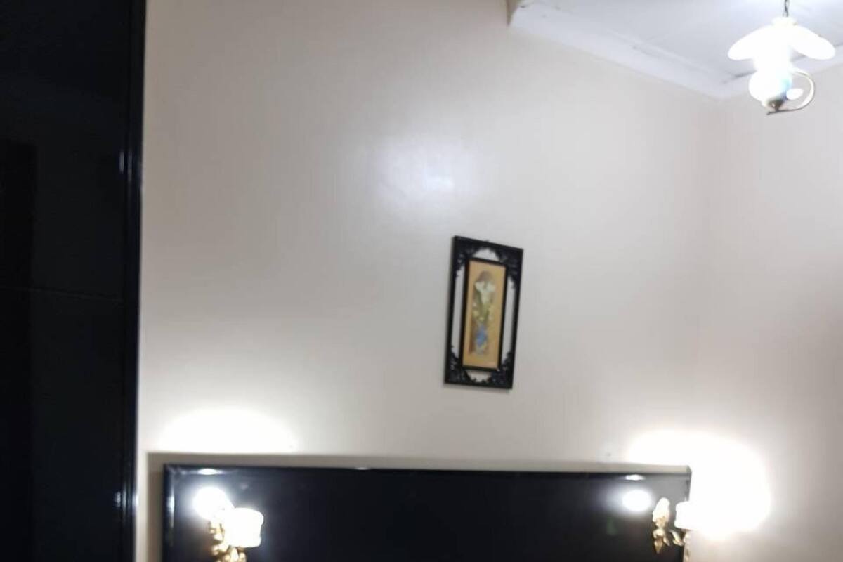 Quarto com cabeceira preta, roupa de cama branca e duas luminárias de cabeceira.