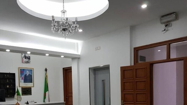Un hall d’entrée avec des sièges en cuir, un comptoir de réception, un lustre et des drapeaux.