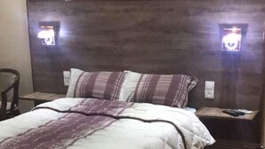 Un lit bien fait, avec une couette matelassée et des oreillers, une tête de lit en bois et deux lampes de chevet.