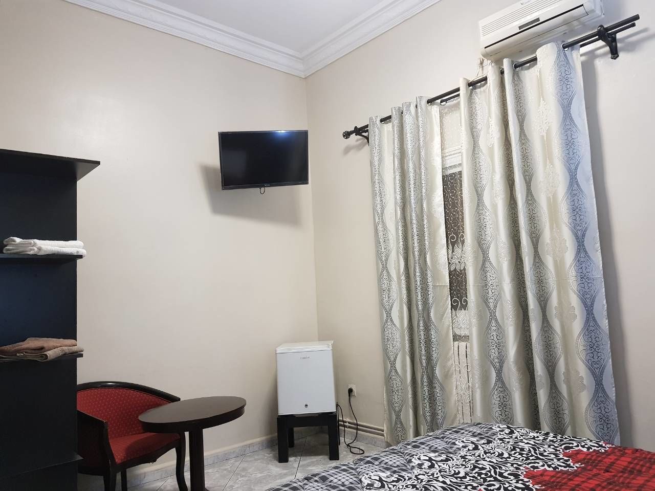 Habitación de hotel pequeña con cama, una mesita, una silla, televisor montado en la pared y un calentador.
