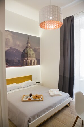 Une chambre d’hôtel avec un lit, un plateau de nourriture, un luminaire suspendu et une grande fresque murale.