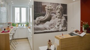 A modern kitchen with white cabinets, a dining area with a red table, and a large wall-mounted artwork of a reclining figure. - Napolinn B&B (Naples)