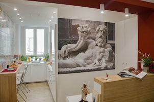 A modern kitchen with white cabinets, a dining area with a red table, and a large wall-mounted artwork of a reclining figure.